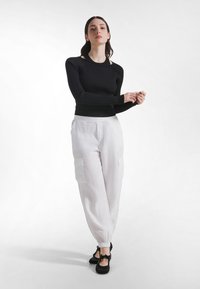 Sort ribstrikket langærmet top kombineret med hvide linned cargobukser med sidelommer og elastiske manchetter, suppleret med sorte sko med sløjfer.