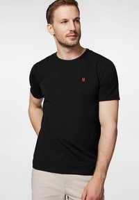 Czarny bawełniany T-shirt z krótkim rękawem i okrągłym dekoltem, z małym czerwonym logo na lewej stronie klatki piersiowej. Gładka tekstura, klasyczny krój.