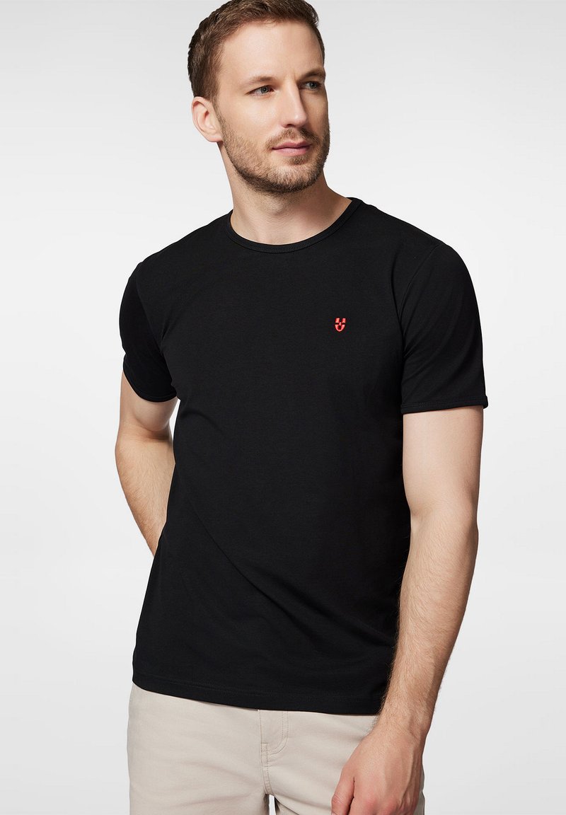 Czarny bawełniany T-shirt z krótkim rękawem i okrągłym dekoltem, z małym czerwonym logo na lewej stronie klatki piersiowej. Gładka tekstura, klasyczny krój.