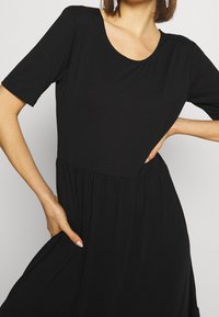 Robe noire à manches courtes avec encolure dégagée, taille froncée et ourlet fluide. Confectionnée en tissu lisse. Dotée de poches latérales.