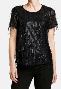 Top nero con maniche corte, caratterizzato da dettagli in frange e paillettes. Il tessuto trasparente aggiunge texture al design. Orlo piatto senza vita definita.