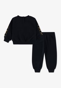 Juodos spalvos sportinė apranga, kurioje yra trumpas džemperis su auksiniais akcentais ant rankovių ir atitinkami siaurėjantys kelnių modeliai su elastingais manžetais.