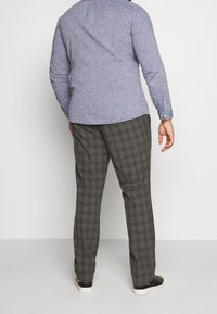 Lichtblauw overhemd met lange mouwen en een subtiele textuur, gecombineerd met grijze geruite broeken. De outfit heeft een relaxte pasvorm en zwarte sneakers.