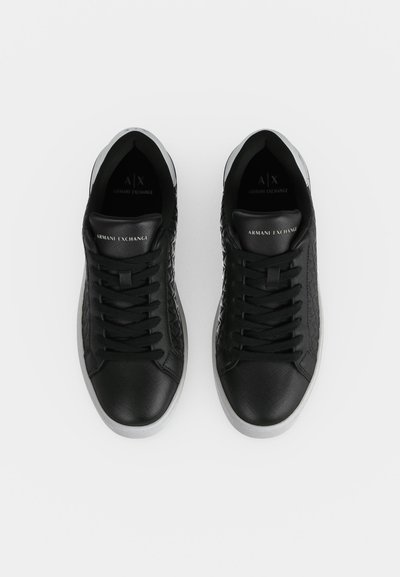 Une paire de baskets noires Armani Exchange à lacets, avec des empiècements texturés et des semelles blanches, vue de dessus sur un fond uni.