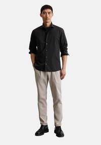 Camicia nera con bottoni, maniche lunghe, pantaloni beige e scarpe nere. La camicia presenta un colletto a punta e un design semplice.