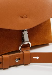 Borsa a tracolla in pelle e suede color marrone chiaro con una chiusura in argento, tracolla regolabile, pattina superiore liscia e corpo testurizzato.