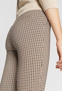 Pouzdrové kárované kalhoty v hnědé, béžové a černé barvě. Texturovaná tkanina s malým kostkovaným vzorem, s bočními kapsami a štíhlým střihem.