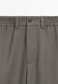 Pantalon gris avec ceinture élastique, fermeture par bouton et passants de ceinture, en tissu texturé.
