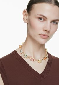 Naszyjnik w kolorze złota z różnokolorowymi kamieniami szlachetnymi, w tym różowym, zielonym i bursztynowym, osadzonymi w owalnych i okrągłych kształtach.