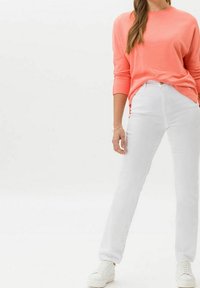 Suéter de manga larga color coral combinado con jeans blancos de pierna recta y zapatillas blancas. La tela parece suave, con un ajuste holgado. Sin patrones visibles.