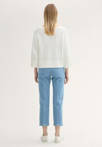 Vit stickad tröja med vida ärmar och strukturerad mönster, kombinerad med ljusblå cropped jeans och vita snörningsfria skor.