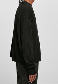 Czarny sweter dzianinowy o luźnym kroju, opadających ramionach, ściągaczach na rękawach i na dole, ukazujący miękką strukturę i minimalistyczny design.