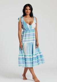 Blå och vit mönstrad maxi-klänning med djup V-ringning, knytband över axlarna och skirtrad kjol med geometriska mönster och textur.