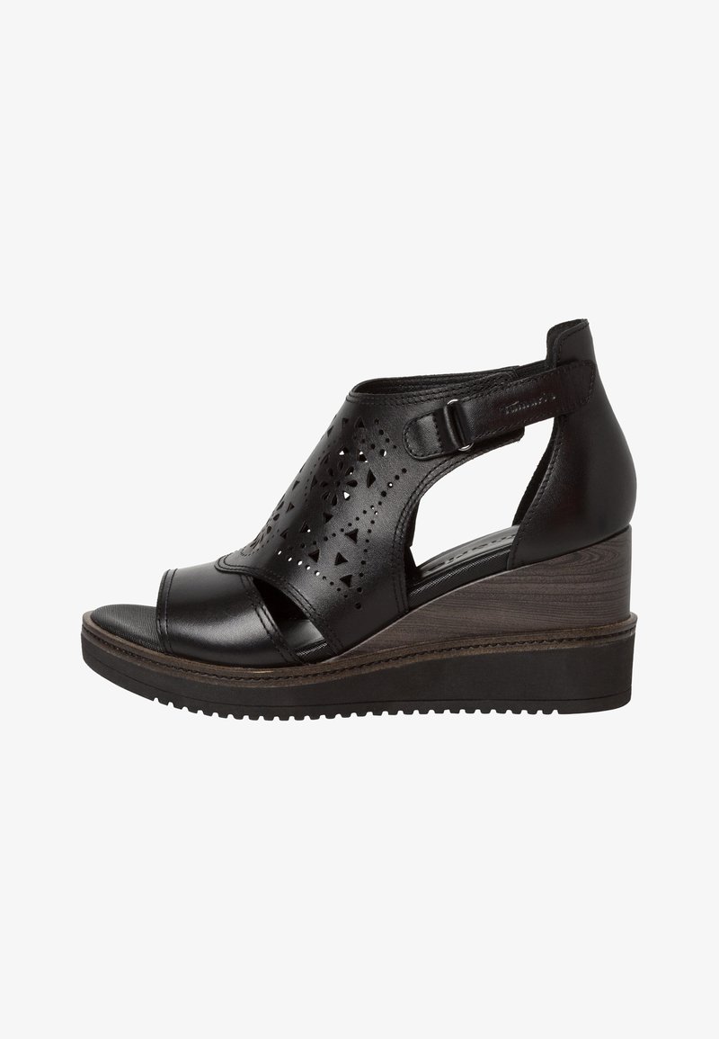 Sandale compensée en cuir noir avec motifs découpés, bride de cheville réglable, bout ouvert et talon compensé texturé. Design légèrement courbé.