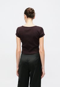 Camiseta de manga corta de color marrón oscuro con un escote redondo y textura acanalada, combinada con pantalones verde oscuro. Vista desde atrás.