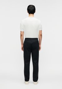 Μαύρο αθλητικό παντελόνι με άσπρες ρίγες στο πλάι, ελαστική μέση και ίσια γραμμή στο πόδι, συνδυασμένο με ένα απλό λευκό εφαρμοστό μπλουζάκι.