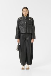 Zwarte leren cropped jacket met gespikkelde schouders, gecombineerd met zwarte wijduitlopende broek. Gecombineerd met een kleine zwarte tas en crèmekleurige open schoenen.