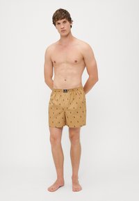 Shorts de baie maron deschis cu modele subtile de polo negre. Curea elastică cu etichetă logo, design până la genunchi, fabricate din material ușor.