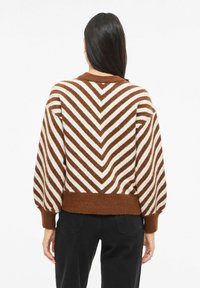 Hnědý a krémový pruhovaný svetr s chevronovým vzorem, nabíranými rukávy a žebrovaným lemem. Měkká textura v pohodlném střihu.