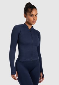 Top de manga larga de cierre tipo zip en color azul marino con textura acanalada, cuello alto y orificios para los pulgares. Diseño ajustado que acentúa la silueta.