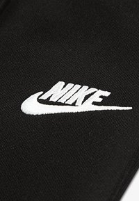 Μαύρο ύφασμα με λευκό κεντητό λογότυπο Nike που περιλαμβάνει το σχέδιο swoosh και χαρακτηριστικά γράμματα. Υφή με επιφάνεια χωρίς μοτίβα.