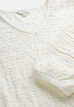 Hvid tekstureret bluse med V-hals, elastiske ærmekanter og dekorativ blonderkant nær kanten.