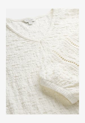 Witte blouse met textuur, V-hals, elastische manchetten en decoratieve kantafwerking bij de manchetten.