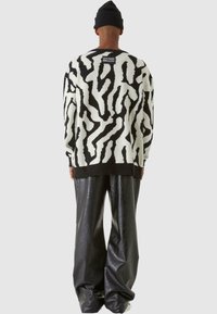 Stickad tröja med ett svart och vitt abstrakt mönster, långa ärmar, ribbade manschetter och fåll, kombinerad med högmidjade svarta glänsande byxor.