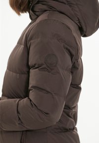 Brązowa kurtka puchowa z pikowanym wzorem, kapturem i okrągłym wytłoczonym logo na lewej stronie ramienia. Gładka, matowa tekstura materiału.