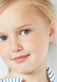 Orecchino a forma di stella rosa con un design a strati, indossato all'orecchio sinistro di un bambino. I capelli del bambino sono biondo chiaro e hanno tratti delicati.