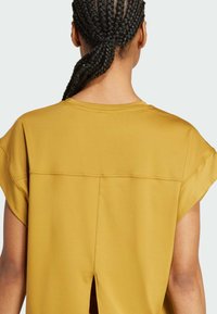 Top amarillo mostaza de mangas cortas con cuello redondo y una pequeña abertura en la parte trasera. Tela suave con un corte holgado y costuras estructuradas.