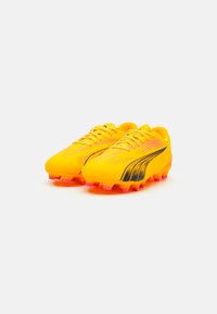 Botas de fútbol de un brillante color amarillo con acentos negros, parte superior texturizada y suelas con tacos. Presenta un diseño elegante y un tradicional cierre con cordones.