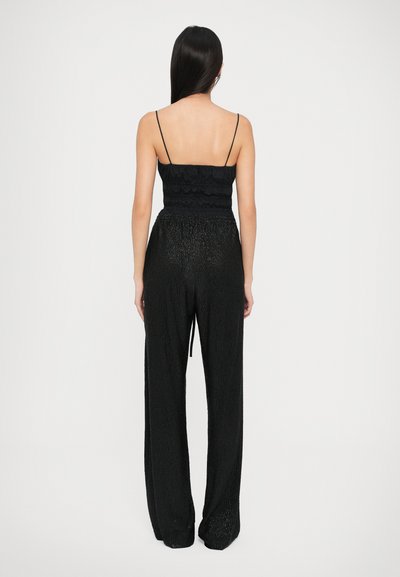 Compleu negru format din două piese, cu un top cu bretele subțiri, plisat, și pantaloni lărgi dintr-un material texturat și lucios, văzut din spate.