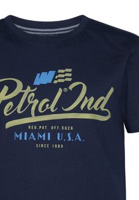 Marinblå t-shirt i bomull med rundad halsringning. Har stor grafisk text: "Petrol Ind" i guld och blått, med detaljer nedanför.