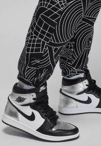 Zwart-wit gestreepte joggingsbroek met geometrische ontwerpen, gecombineerd met zilver- en zwarte hoge sneakers met een witte swoosh-logo.