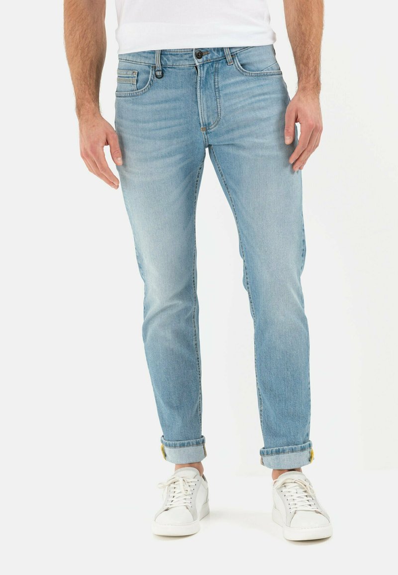 Light blue denim jeans with a slim fit and rolled cuffs, featuring a classic five-pocket design and subtle stitching details. Paired with white sneakers.