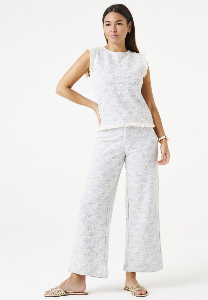 Tweedelig ensemble met een mouwloze, gestructureerde top en wijde broek in lichtblauwe en witte tinten, met franjes langs de randen.
