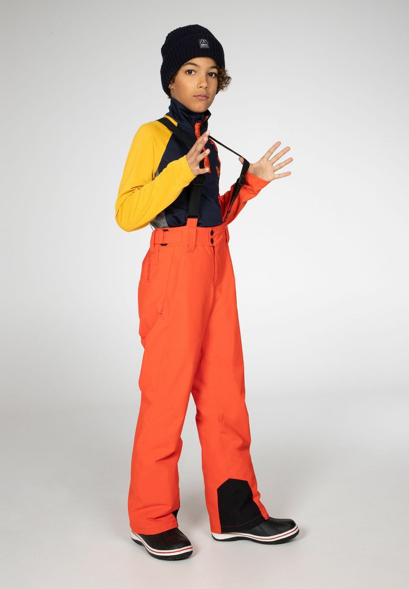 Heldere oranje skibroek met verstelbare bandjes, gecombineerd met een marineblauw en gele top. Zwarte sneeuwlaarzen maken de outfit compleet. Gladde stofstructuur.