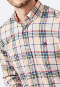 Camisa de cuadros abotonada en color crema, con líneas rojas, azules y verdes. Tejido suave, cuello estándar y logo en el pecho.