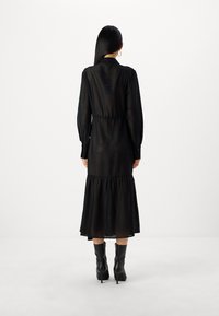 Musta pitkähihaisessa mekossa on teksturoitu verkkomuotoilu, kerroksellinen helma ja tiukka vyötärö. Yhdistetty polven yli ulottuviin mustiin nahkasaappaisiin.