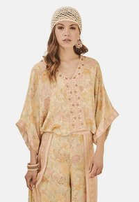Top ligero de tono pastel con estampado floral, escote en V, mangas oversize y botones decorativos. Combina con pantalones florales a juego.