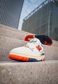 Baskets en cuir blanc avec des accents rouges et bleus, une semelle texturée et un col rembourré. Présentent un grand logo "N" rouge et une languette en maille.