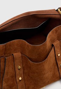Interno della borsa in pelle scamosciata marrone con due scomparti curvi. Finiture in oro sull'abbottonatura. Superficie morbida e testurizzata con fodera nera.