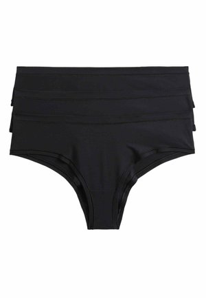 Kobieta w czarnych spodenkach od bikini i czarnym topie, widziana od talii do górnej części ud na białym tle.