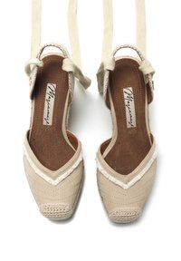 Scarpe espadrillas beige con design a forma di V, texture intrecciata sulla punta, dettagli in frange e lacci alla caviglia.