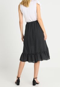 Černá sukně s puntíky a volánovým lemem. Vyrobena z lehké látky s elastickým pasem a kombinovaná s bílým topem.