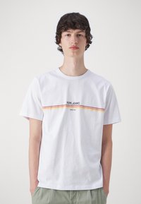 Fehér pamut póló, vízszintes csíkozással piros, narancssárga és sárga színekben, alatta a "PEPE JEANS" és a "SINCE 1973" felirattal.