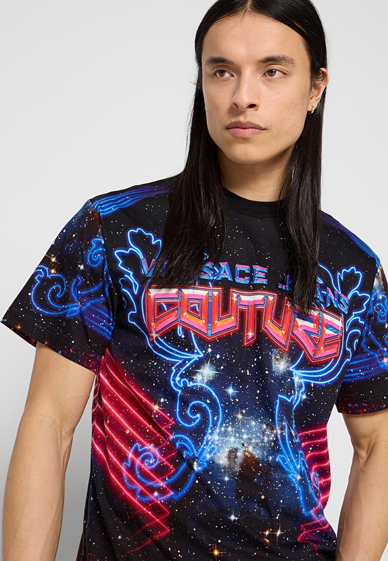 Camiseta negra con estampado de galaxia, con acentos en azul y rojo neón. El logo centrado dice "Versace Jeans Couture" de manera destacada.