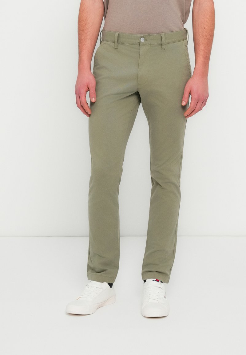 Χακί παντελόνια chinos από βαμβακερό μείγμα, με στενή γραμμή, μπροστινές τσέπες, κλείσιμο με κουμπιά και λείο φινίρισμα. Συνδυασμένα με λευκά αθλητικά παπούτσια.