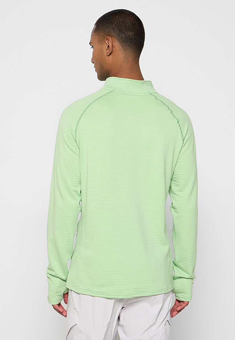 Chemise longue à manches longues vert clair avec un tissu texturé, des coutures plates et un col montant. Dotée de manches raglan pour faciliter les mouvements.